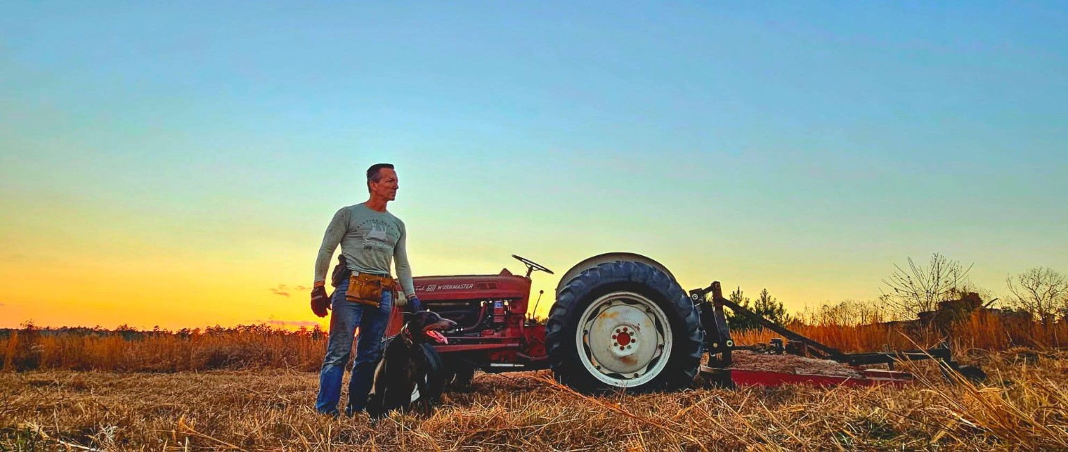 Tim and his dog Bleu standing beside the Ford 601 tractor at sunset